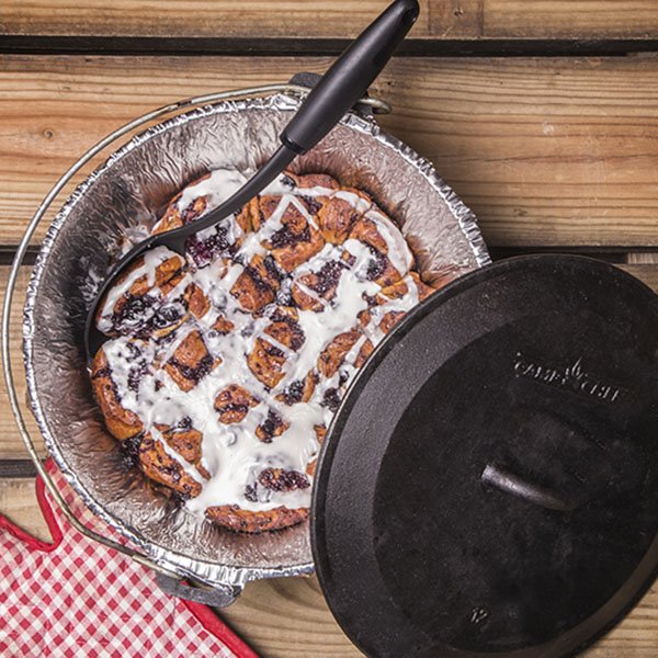 Fresh off the fire and frosted Dutch Oven Blueberry Cinnamon Rolls served on a picnic table.