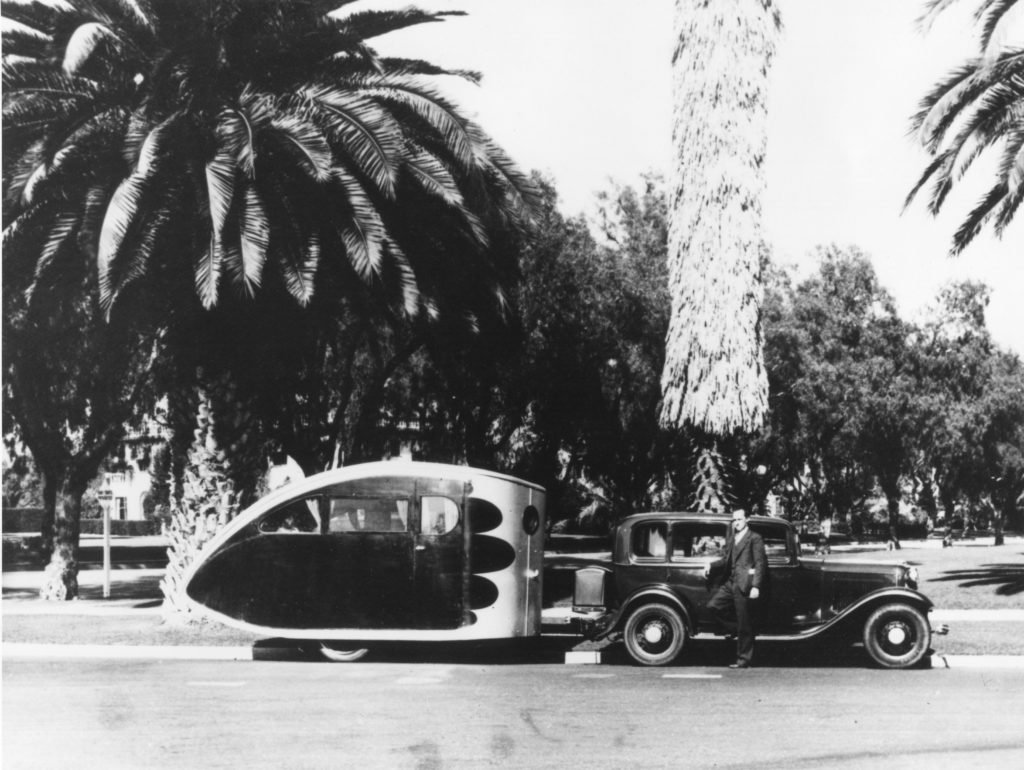 This photo shows an early Airstream trailer, probably created around 1933. This man appears to be Wally Byam even though he is not identified. The early Airstream trailers were shaped like a “teardrop” to improve aerodynamic efficiency, and the sleeping compartment in this model sits toward the rear of the trailer.