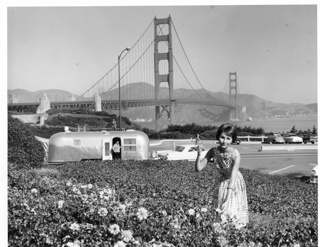 Stopping to pick flowers in San Francisco in 1964, with the Golden Gate Bridge as a backdrop. The car is a 1964 Cadillac, and the trailer is an Airstream Land Yacht.
