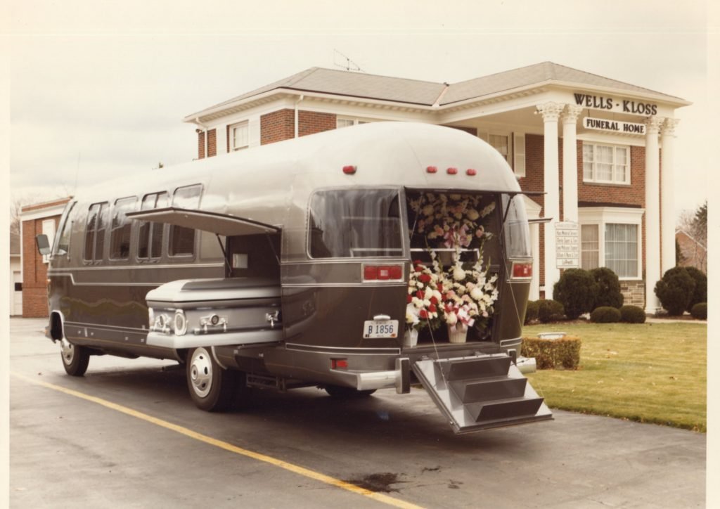 This is an exterior view of an Airstream Funeral Coach around 1982. The flowers were put in the back and the casket was put in a side carrier space. Mourners could ride inside the passenger space - with individual seats and a couch.