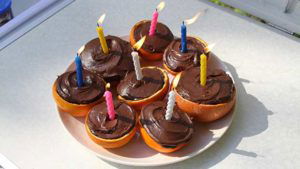 Campfire birthday cake cupcakes in citrus halves - oranges and grapefruit - with candles lit, ready for the party to begin.