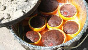 Campfire birthday cake cup cakes in citrus halves being checked after 15 minutes on the fire.