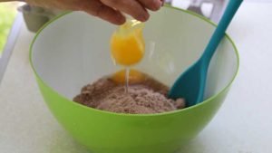 Breaking an egg into the batter for campfire birthday cake cupcakes in citrus halves.