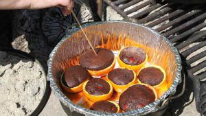 Inserting a wooden skewer into the center of the largest campfire birthday cake cupcakes in citrus halves.