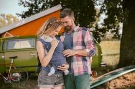 Smiling couple with baby in in front of van in the nature