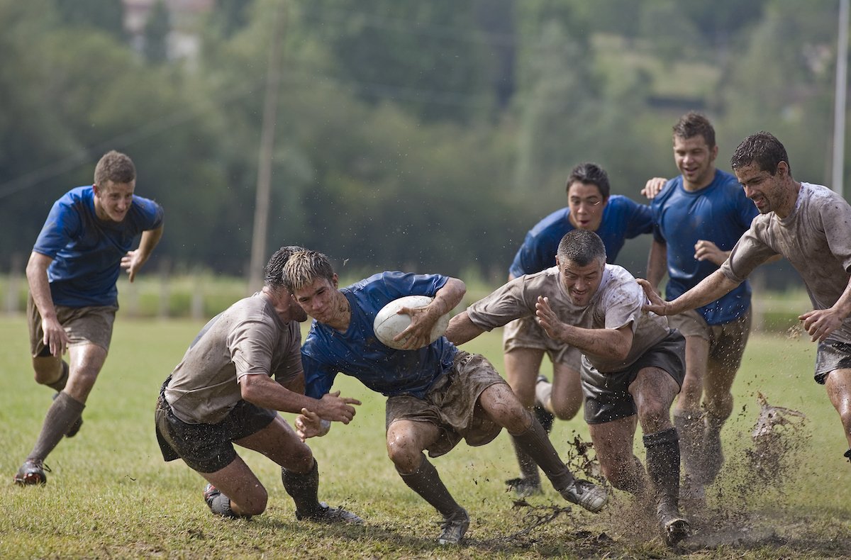 Rugby players covered with mud, tackling opponent