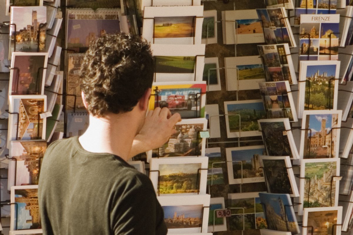 Rear view of a man choosing postcards, Piazza Della Cisterna, San Gimignano, Siena Province, Tuscany, Italy
