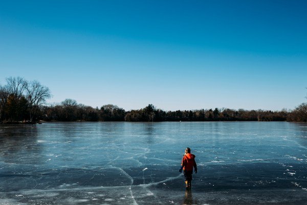 Rear view of carefree boy walking on frozen lake against clear sky during winter