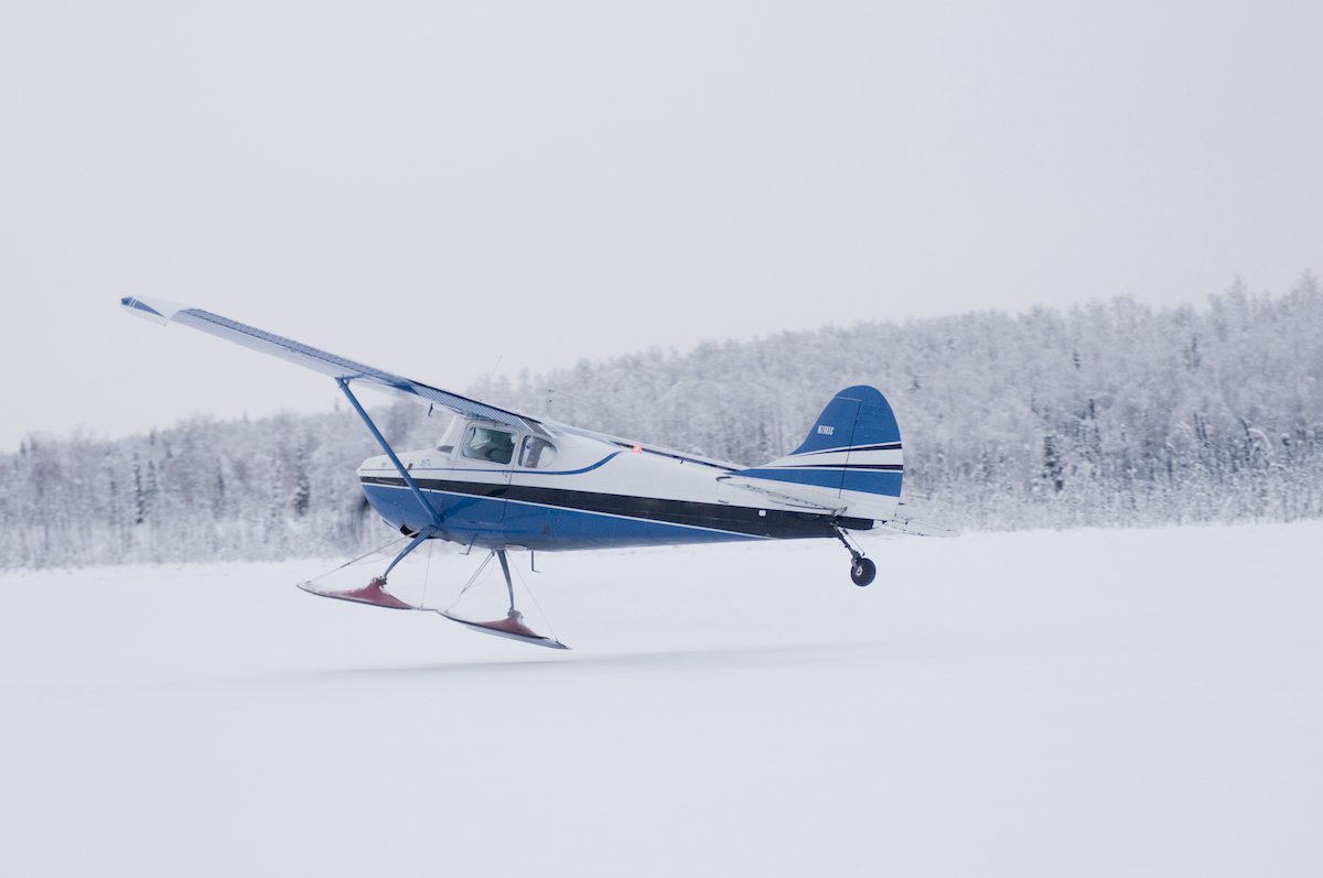 Alaska bush pilot flying a Cessna 170 airplane with skis, winter, taking off from a frozen lake, Alaska