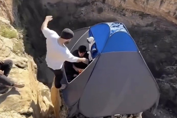 men jump into tent on cliff